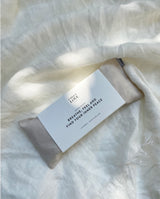 Augenkissen "breath, feel & find your inner peace" in creme liegt mit Banderole auf einer leichten Leinendecke.