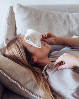 Augenkissen "breath, feel & find your inner peace" in Anwendung. Frau liegt auf einem Sofa und legt sich das Kissen in creme während einer Meditation auf die Augen.