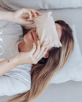 Augenkissen "breath, feel & remember your strenght" in Anwendung. Frau liegt und legt sich das Kissen in hellgrau während einer Meditation auf die Augen.
