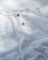 Nahaufnahme des Babybody aus Musselinstoff. Zwei Holzknöpfe am Kragen werden von einer zarten Stickerei gesäumt.