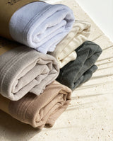 Zusammengerollte und gestapelte Badeponchos für Kinder in fünf Farbvarianten: weiß, creme, soft sand, warm beige, graphite.