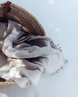 Der Badeponcho in sand liegt in einem Korb. Der Hamam-Stoff hängt hierbei über dem Rand des Holzkorbes.