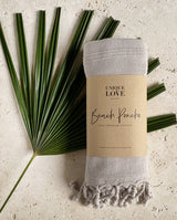 Badeponcho aus Hamam-Stoff für Babys und Kleinkinder in sand gefaltet mit einer Banderole liegt auf einem Palmenblatt.