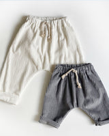 Zwei Pumphosen für Babys und Kleinkinder: Eine kleinere Größe aus hellgrauem Cordstoff und eine größere aus Cord in off white; beide mit aufgesetzter Schnürung am Bund.