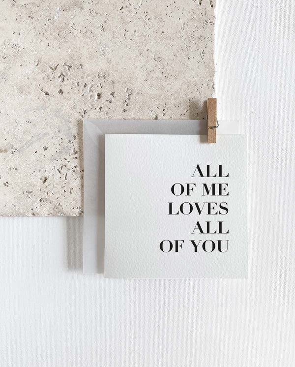 Quadratische Grußkarte zum Klappen mit milchigem Briefumschlag und Holzklemme. Spruch: "All of me loves all of you"