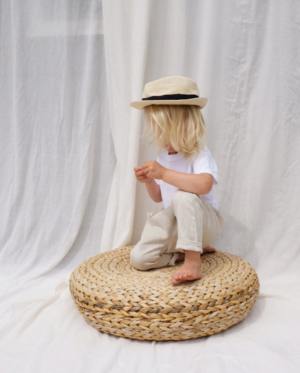 Ein Kleinkind sitzt auf einem runden Holzkissen und trägt die Leinenhose in creme.