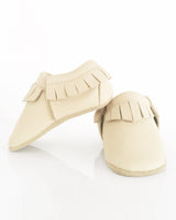 Moccasins – Lederschuh für Babys und Kleinkinder mit Fransen am oberen Bündchen in hellem creme in der Front- und Seitenansicht.