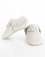 Moccasins – Lederschuh für Babys und Kleinkinder mit Fransen am oberen Bündchen in weiß in der Front- und Seitenansicht.