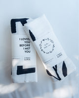 Zwei Musselintücher, die zusammengefaltet sind und mit einer Banderole umwickelt sind. Sprüche: "I loved you before I met you" und "Hello Little one".