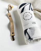 Musselintuch mit Banderole, die einen Hinweis auf den Schriftzug "Hello Little one" gibt. Neben dem Musselintuch liegt ein Leder Schnullerband in der Farbe hellbraun.