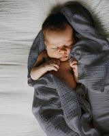 Baby liegt auf Musselindecke in grau und schläft.