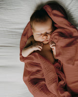 Baby liegt auf Musselindecke in terrakotta und schläft.