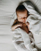 Baby liegt auf Musselindecke in weiß und schläft.