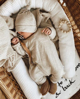 Ein Baby liegt in einem Holzkörbchen und hat einen Schnuller im Mund, der an einem Leder Schnullerband in der Farbe hellbraun befestigt ist.