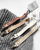 Kollektion der vier Schnullerbänder aus Leder in de Erdfarben, die auf einer grauen Strickdecke liegen.