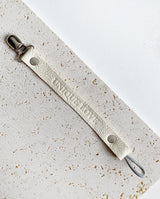 Schnullerband aus Leder in der Farbe creme mit geprägter Aufschrift „UNIQUE LOVE“.