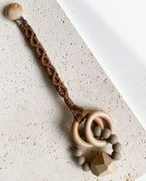 Schnullerband aus Stoff im Makramee Design mit Holzclip in der Farbe dunkelbraun mit einem Spielzeug Greifling daran.