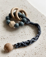Schnullerband aus Stoff im Makramee Design mit Holzclip in der Farbe dunkelgrau mit einem Spielzeug Greifling daran.