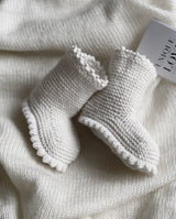 Nahaufnahme der Strickschuhe Boots in creme, die auf einer Decke liegen.