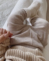 Ein Baby auf dem Schoß der Mama trägt die Strickschuhe creme mit Häkelkante an den Füßchen.