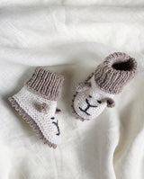 Strickschuhe für Babys in creme mit sand farbener Häkelkante und Bündchen und mit Löwengesicht-Detail in der Detailansicht.