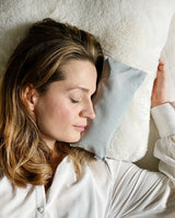 Frau schläft neben dem Augenkissen in hellgrau, das auf Kopfhöhe neben ihr liegt, um so die Entspannung des Kissens zu spüren.