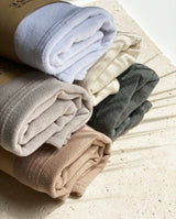 Zusammengerollte und gestapelte Badeponchos für Kinder in fünf Farbvarianten: weiß, creme, soft sand, warm beige, graphite.