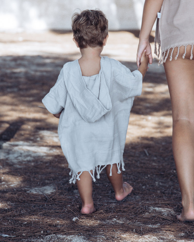 Eine Frau hat ein Kleinkind an der Hand und beide tragen den Strandponcho in der Farbe sand. Für die Erwachsene ist der Poncho ein lässiges Top.