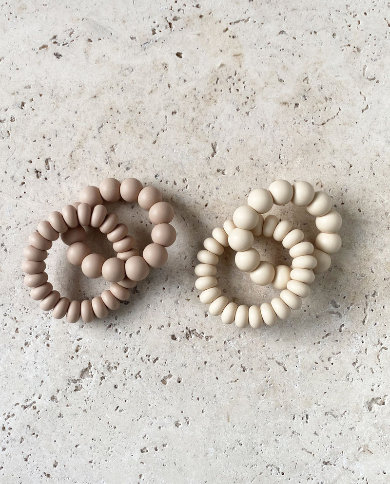 Kollektion aus zwei Greiflingen aus je zwei Ringen mit unterschiedlich großen Silikonperlen in der Farbe pure oat und pure sand.