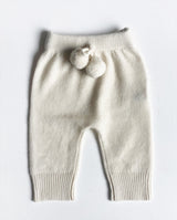 Baby Pumphose aus Cashmere mit zwei Bommeln am Bund in creme liegt auf einer Leinendecke.