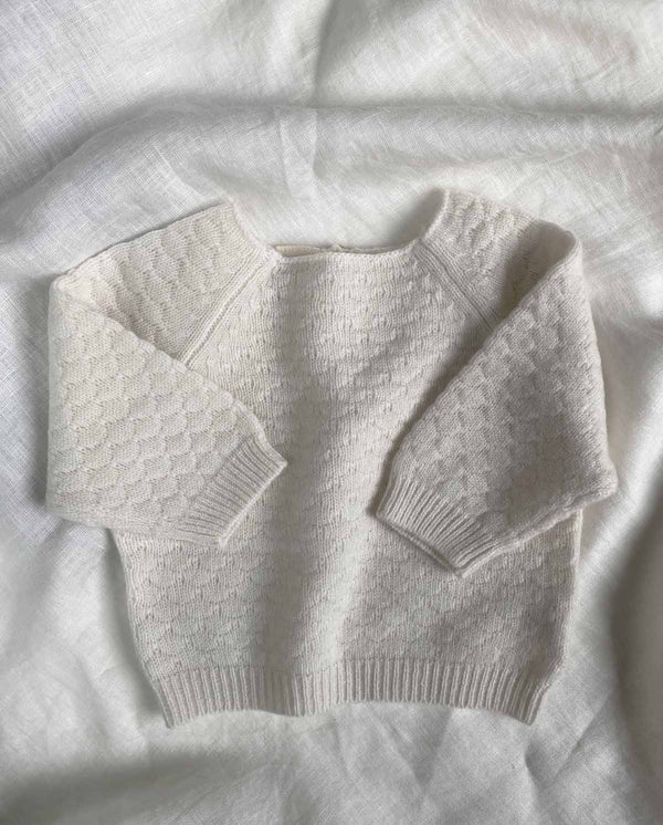 Baby Sweater mit Wabendesign aus Cashmere in creme liegt auf einer Leinendecke.