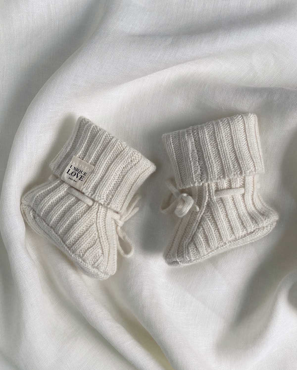 Paar gestrickte Cashmere Babyschuhe in creme mit Schnürung und UNIQUE LOVE Label.