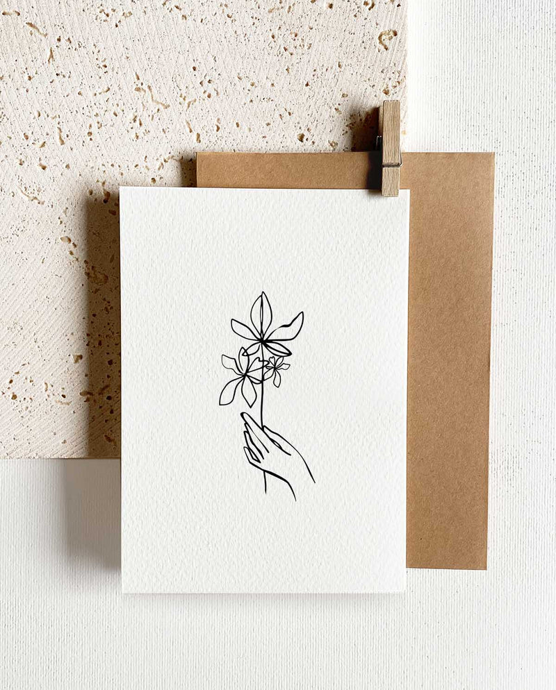 Rechteckige Grußkarte zum Klappen mit braunem Briefumschlag und Holzklemme. Illustration in Skizzenform: Hand hält einen Blumenstrauß