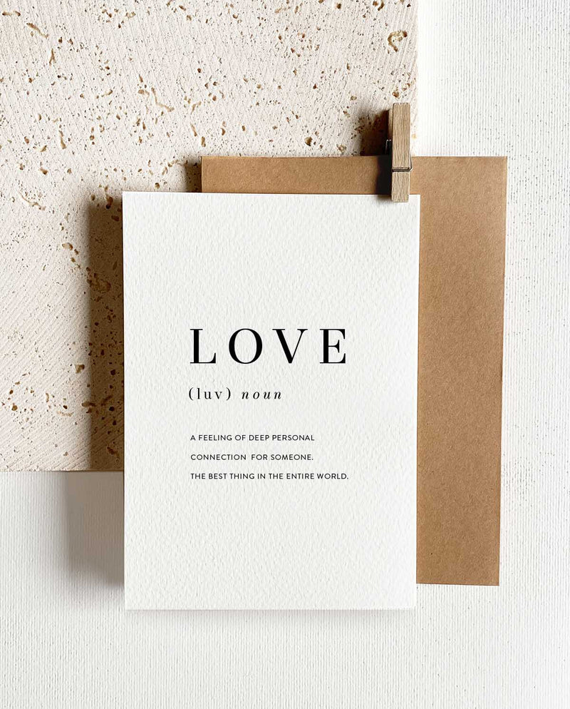 Rechteckige Grußkarte zum Klappen mit braunem Briefumschlag und Holzklemme. Abgebildet ist in schwarzer Schrift die Definition von LOVE.
