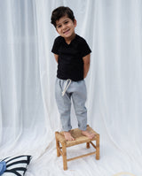 Kleiner Junge steht auf einem Holzhocker und trägt die Leinenhose in hellgrau mit der Schnürung am Bund. 