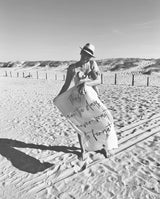 Eine Mama steht mit ihrem Baby auf dem Arm am Strand und hält das Musselintuch ausgebreitet, sodass der Schriftzug "These are the days I never want to forget" lesbar ist.
