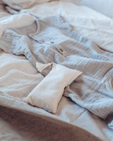 Musselin Overall für Babys in grau liegt zusammen mit einem Kinder Duftkissen Lavendel in creme auf einem Betz.t.