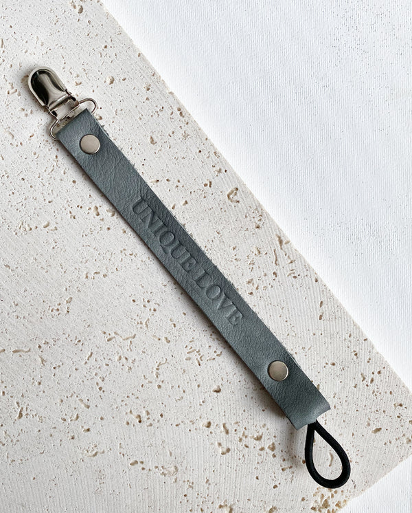 Schnullerband aus Leder in der Farbe grau mit geprägter Aufschrift „UNIQUE LOVE“.