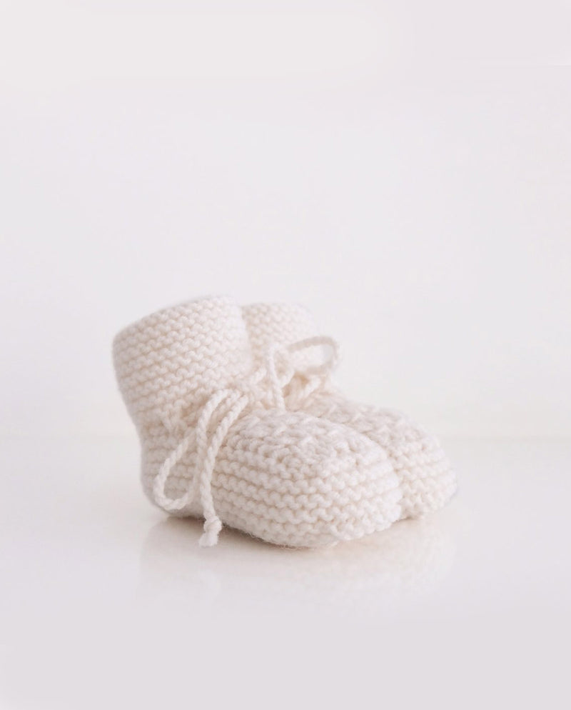 Strickschuhe für Babys in der Farbe off white mit einer Schleife zum Schnüren.