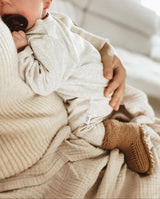 Ein Baby auf dem Arm eines Erwachsenen trägt die Strickschuhe Caramal an den Füßchen.