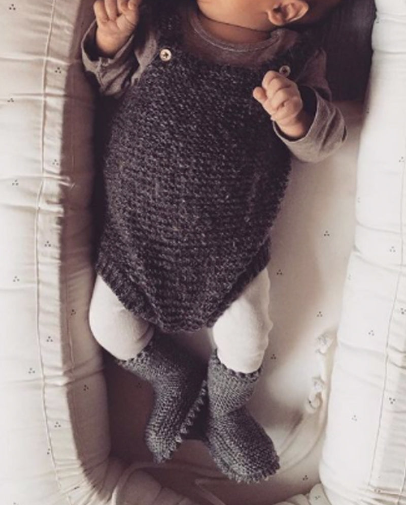 Ein Baby liegt in einem Baby Nestchen und trägt neben einem Strick Body die Strickschuhe in dunkelgrau mit Häkelkante an den Füßchen.