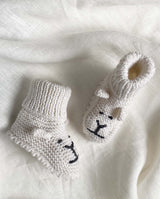 Strickschuhe für Babys in creme mit Löwengesicht-Detail und Häkelkante in der Detailansicht.