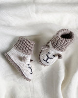  Strickschuhe für Babys in creme mit sand farbener Häkelkante und Bündchen und mit Löwengesicht-Detail in der Detailansicht.