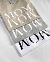 Nahaufnahme des Schriftzugs MOM WOW auf den drei übereinander gefalteten Baumwoll- T-Shirts.