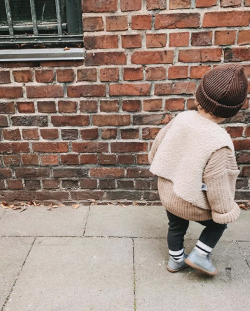 Ein Kleinkind trägt die aus veganem Material gefertigte Weste für Kinder zum Wenden über einem dicken Wollpullover.