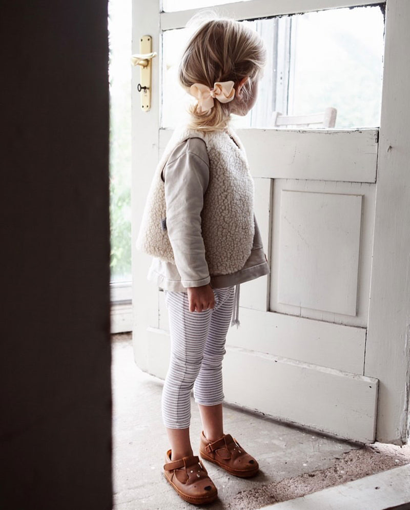 Ein Mädchen trägt die Kinderweste in der Wendefunktion. Das eigentliche Innenfell in creme trägt sie außen und die glatte vegane Lederzeite innen.